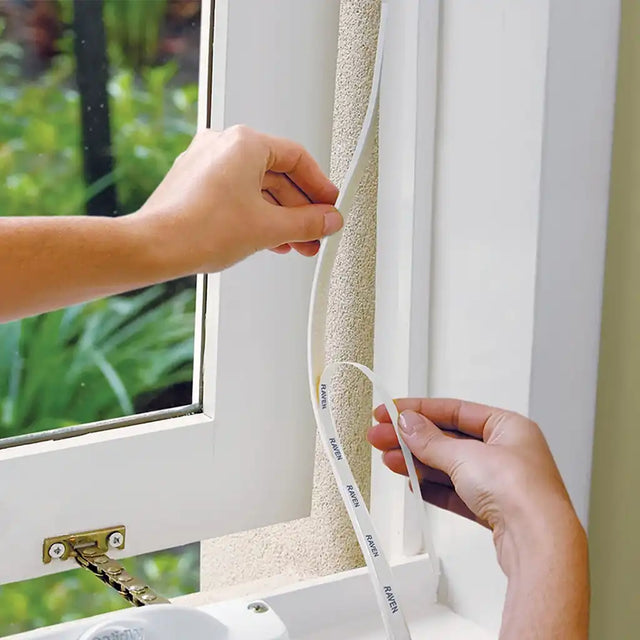 Person applying weather stripping to a window