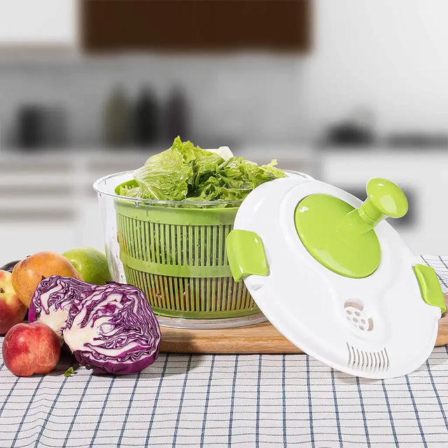 Green and white kitchen tool on a checkered tablecloth with fruits and vegetables.