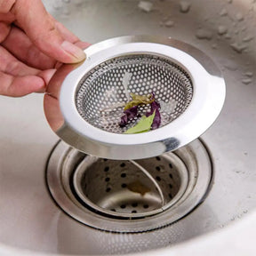 Hand holding a metal sink strainer over a clogged sink drain.