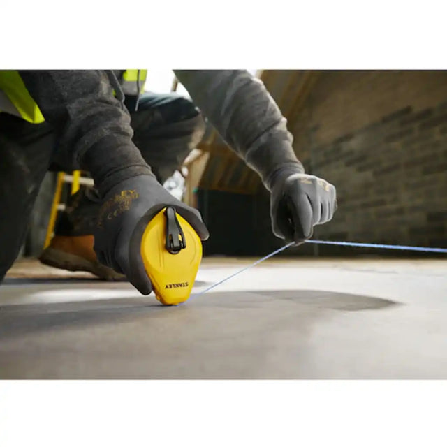 Tradesperson using Stanley chalk line reel to snap a line on a concrete floor
