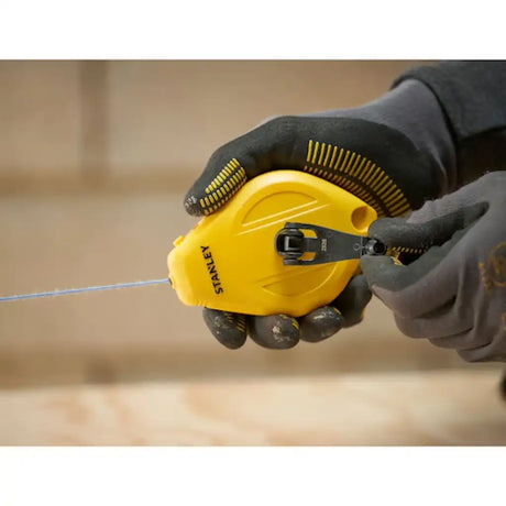 Close-up of hands holding Stanley chalk line reel with line extended

