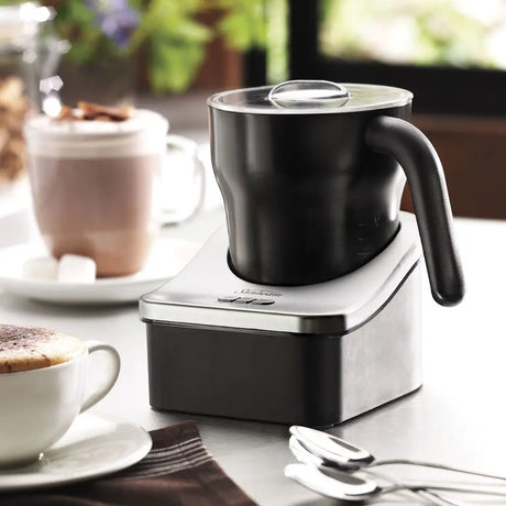 Black milk frother on a white base with a cup of coffee and hot chocolate in the background.