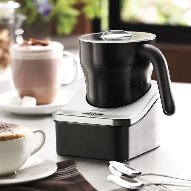 Black milk frother on a white base with a cup of coffee and hot chocolate in the background.