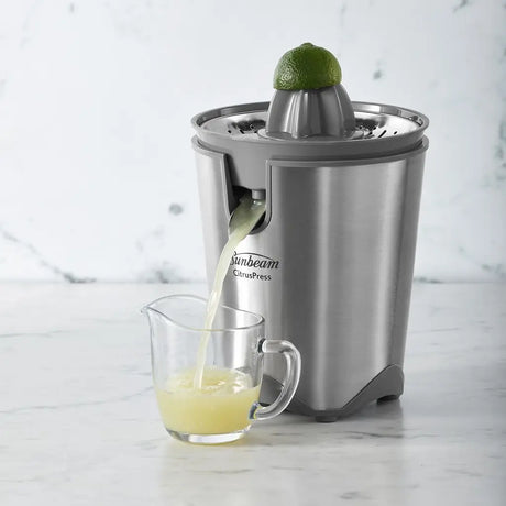 Sunbeam citrus press juicing a lime with juice collected in a glass on a marble surface.
