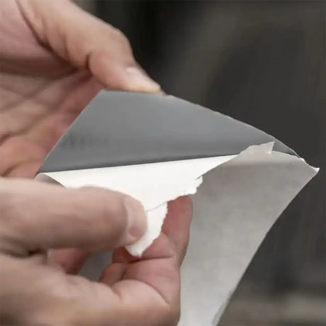Person peeling back a piece of gray tape from white paper