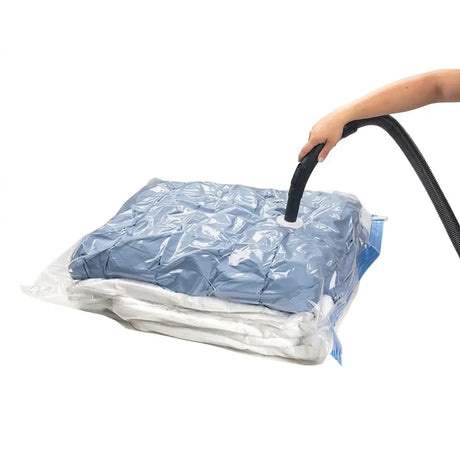 Person using a vacuum cleaner to compress clothes in a clear plastic bag on a white background