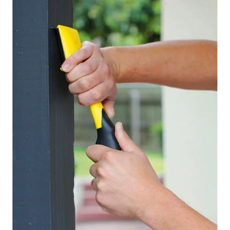 Person using a yellow and black tool on a dark surface with a blurred outdoor background