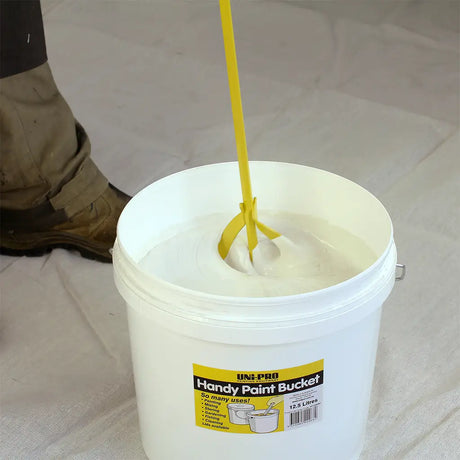 White paint bucket with yellow paint being poured into it, on a white background.