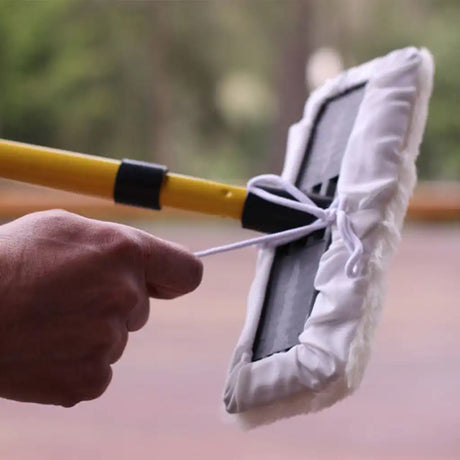 Hand holding a squeegee with a white cloth over a blurred outdoor background