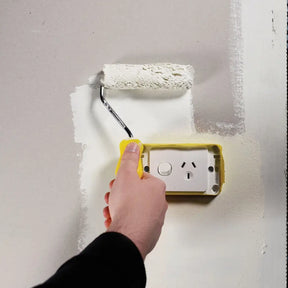 Person painting a wall with a roller near an electrical outlet.