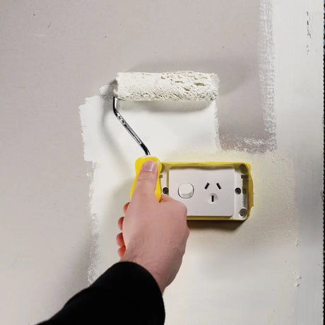 Person painting a wall with a roller near an electrical outlet.
