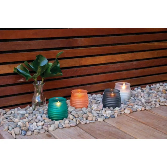 Colorful candles in glass holders on pebbles with a wooden background