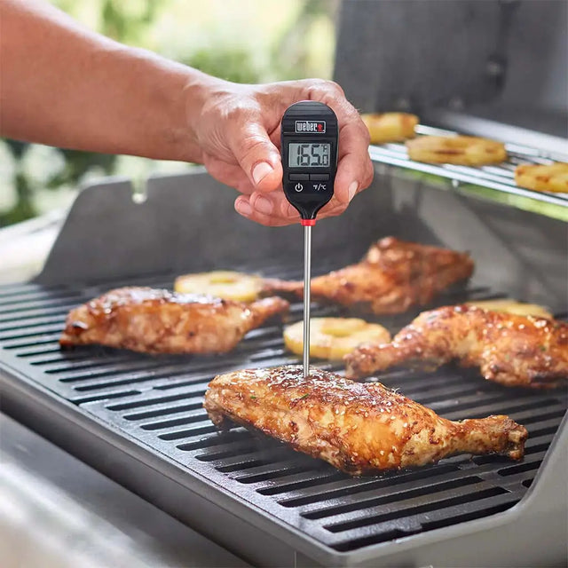 Person using a digital thermometer to check the temperature of grilled chicken on a barbecue.