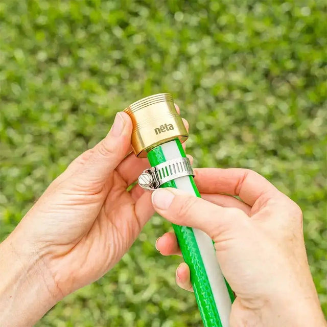 Person holding a green garden hose with a gold fitting against a grassy background