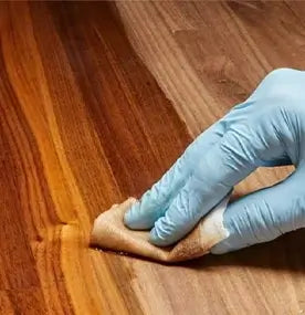 Hand wearing a blue glove cleaning a wooden floor with a cloth.